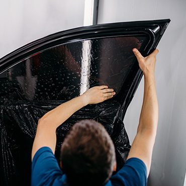 Installer smoothing dark tint film onto a car door window