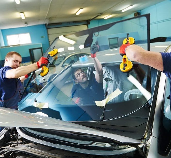 Two technicians lifting a windshield into place with suction cups